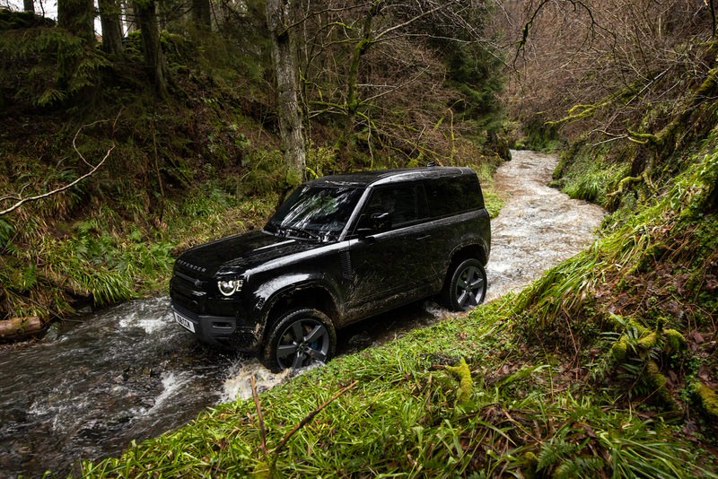 New Land Rover V8 Defender driving in the middle of a mountain stream surrounded by trees