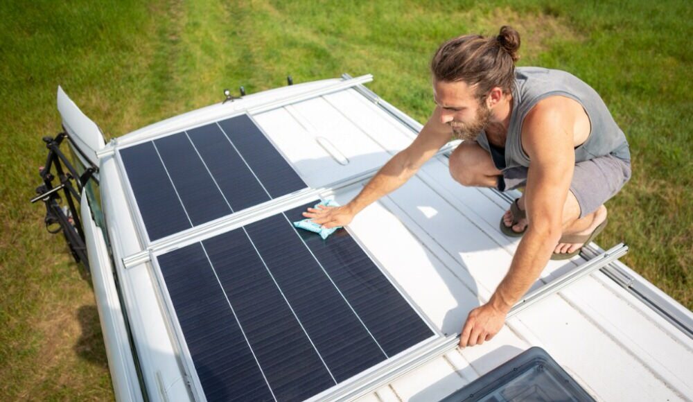 Man cleaning solar panels on top of a Van
