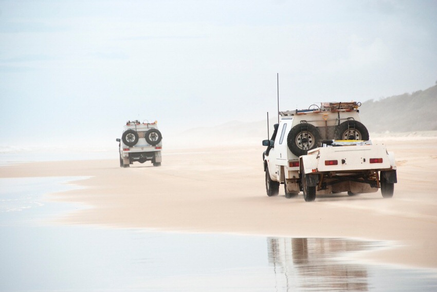 Two SUVs driving in the sand by a river