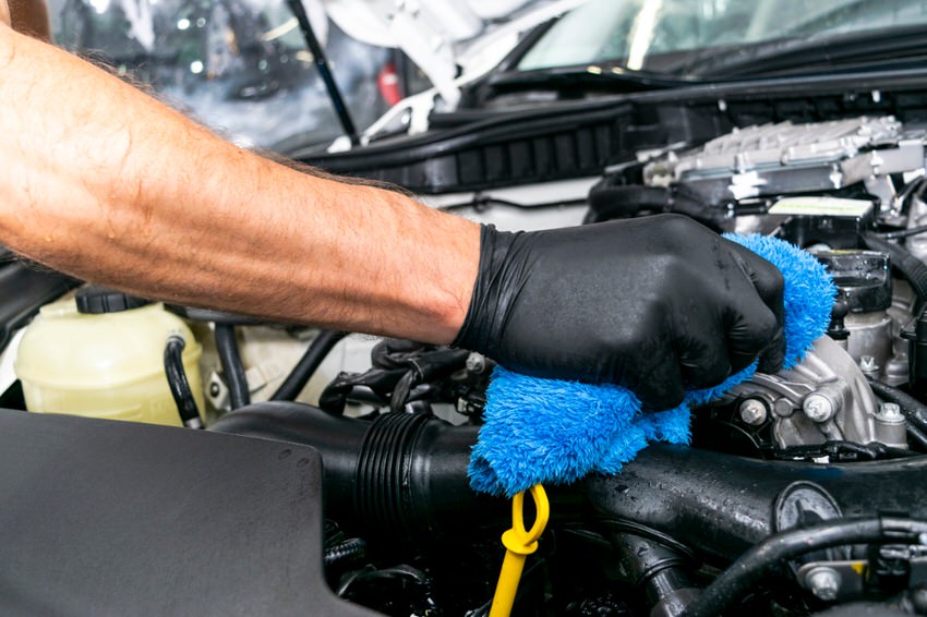 hand wearing a black latex glove cleaning a car engine with a blue rag