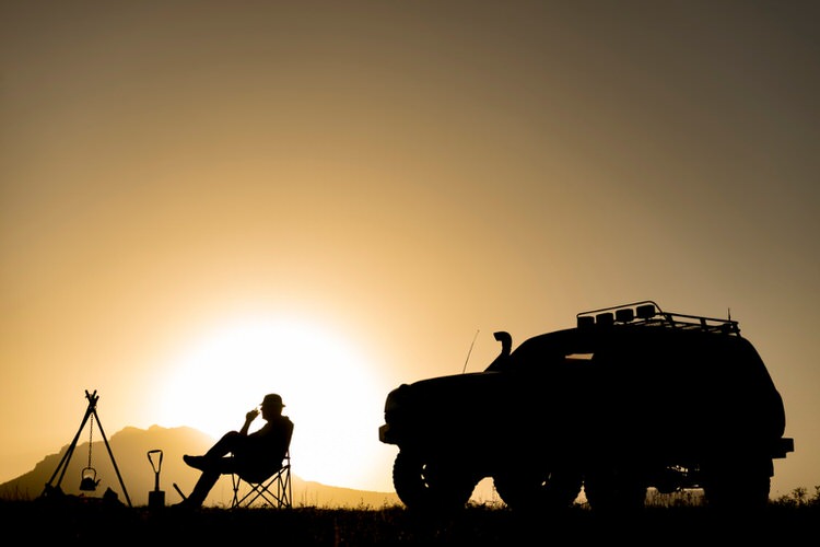 Silhouette of a Person sitting by a fire with their 4x4 overland camping