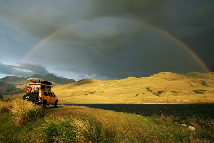 Overlanding Van parked next to a river under a rainbow