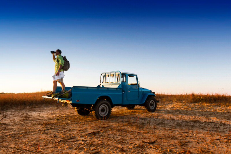 Man standing in 4x4 truck bed holding a map and looking through binoculars