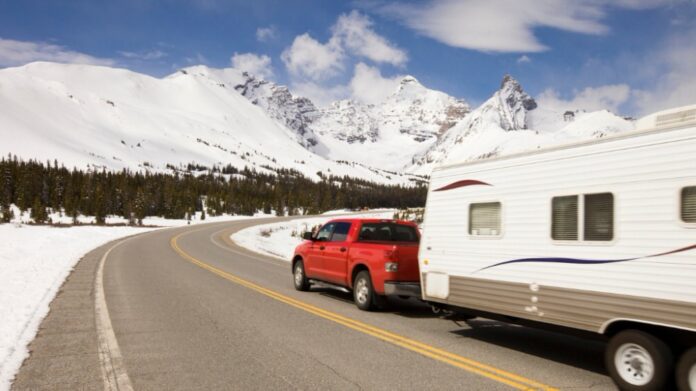 red truck towing camping trailer though snowy mountains