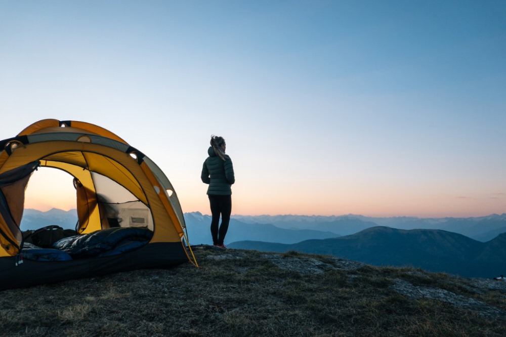 Person standing next to a ground camping tent at sunrise