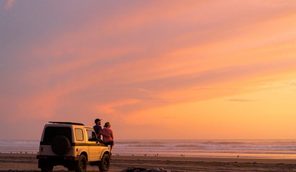 couple by a 4x4 looking at the ocean at sunset