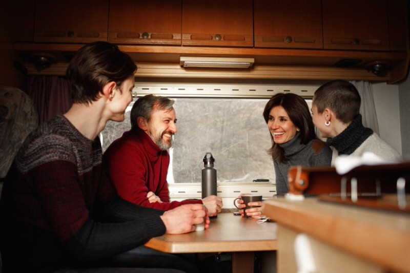 four people enjoying coffee at a table in a travel trailer