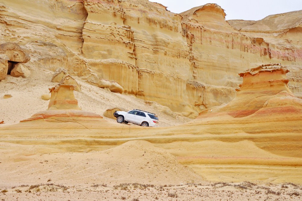 SUV Driving up a sandy hill near rockformations