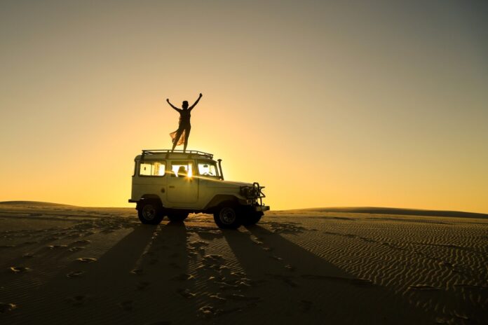 Silhouette of a woman standing on SUV on a solo Overlanding trip