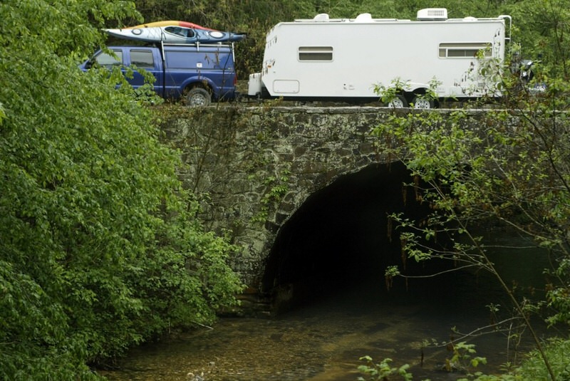 SUV towing camper over small stone bridge