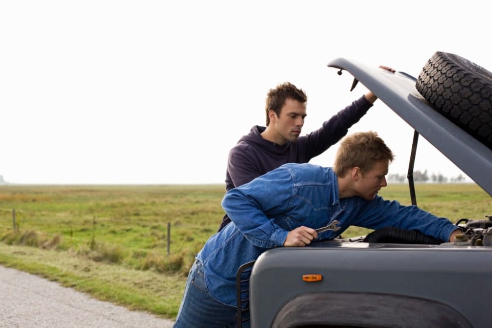 Two boys fixing a truck on the side of the road
