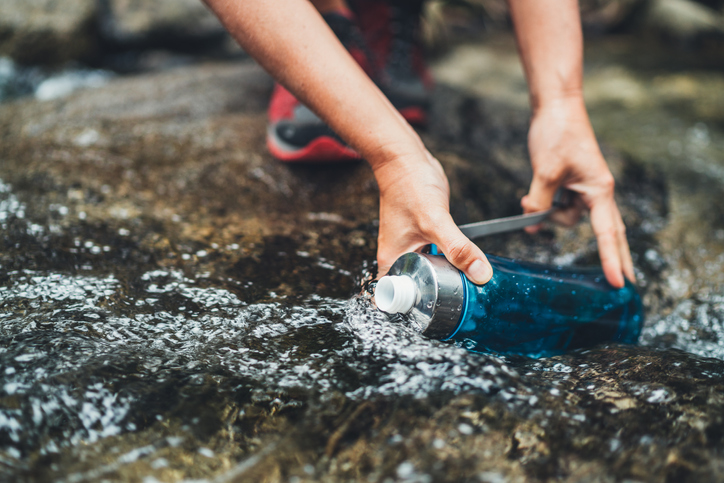 Close-up photo of female hands filling up a water bottle in a stream 