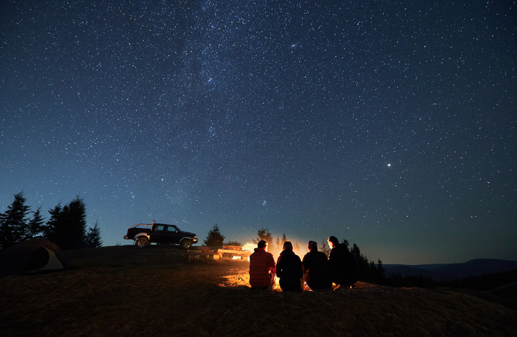 Group of hikers sitting near campfire under night starry sky.