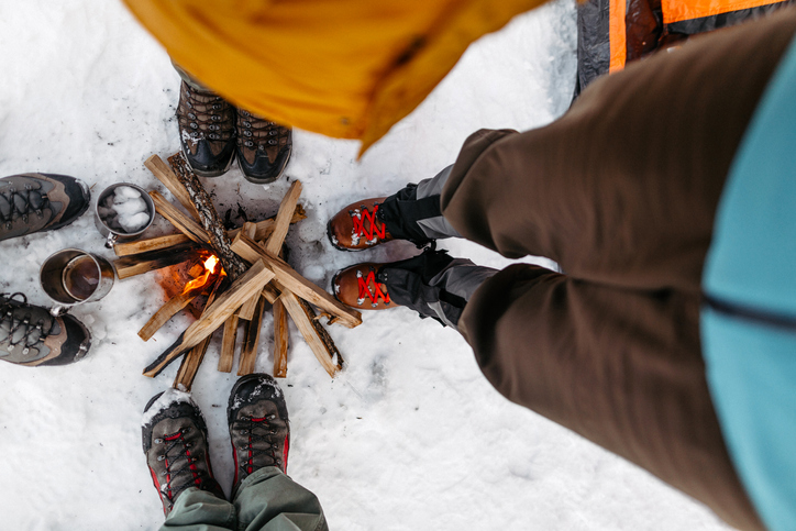 Tourists warming by campfire on snow during winter vacation