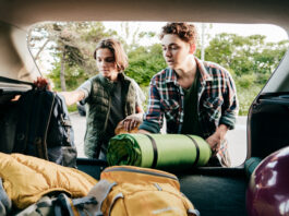 Siblings loading the car for a trip together. Brothers putting backpacks and hiking mats in the car.