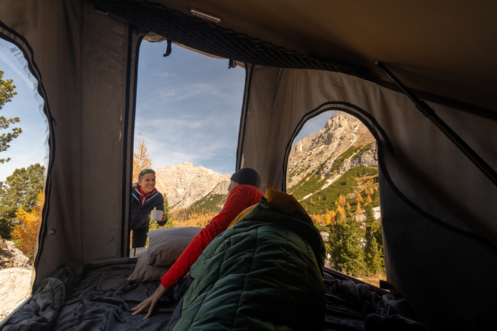 Happy hiking couple on camping vacation with their car and roof top tent in the mountains