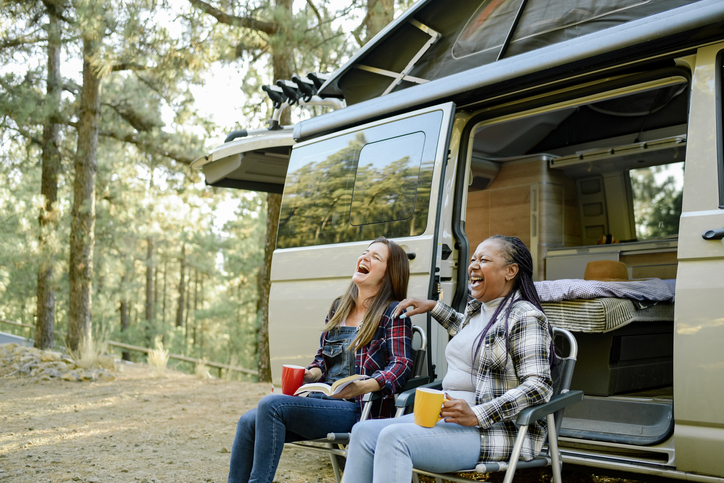 Multiracial traveling women laughing near camper as they experience the benefits of camping