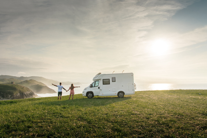 Young couple traveling with their motor home standing by the sea with arms raised