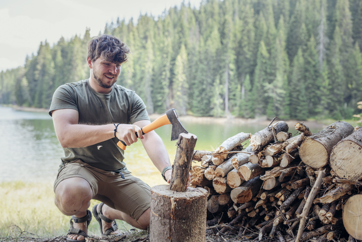 Young man using axe to chop some wood for the campfire.