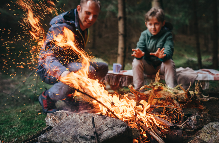 Father and son warms near campfire in forest