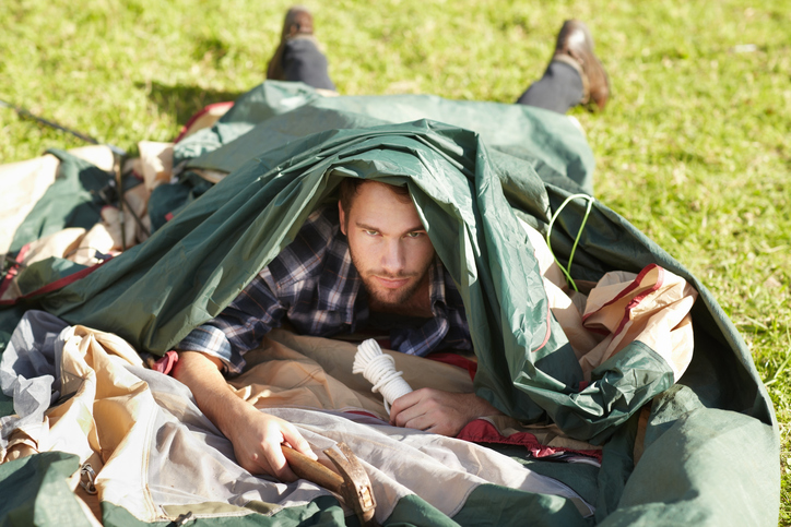 young man struggling to erect a tent outdoors