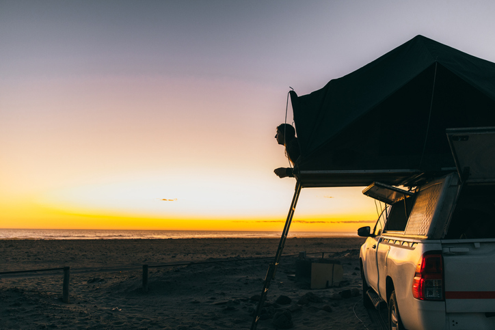 Woman contemplating the scenic sunset at the beach with roof tent camper car in Namibia