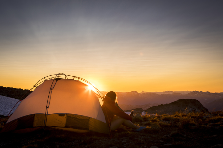 Adventurous woman watching sunset from tent in Whistler backcountry mountains.