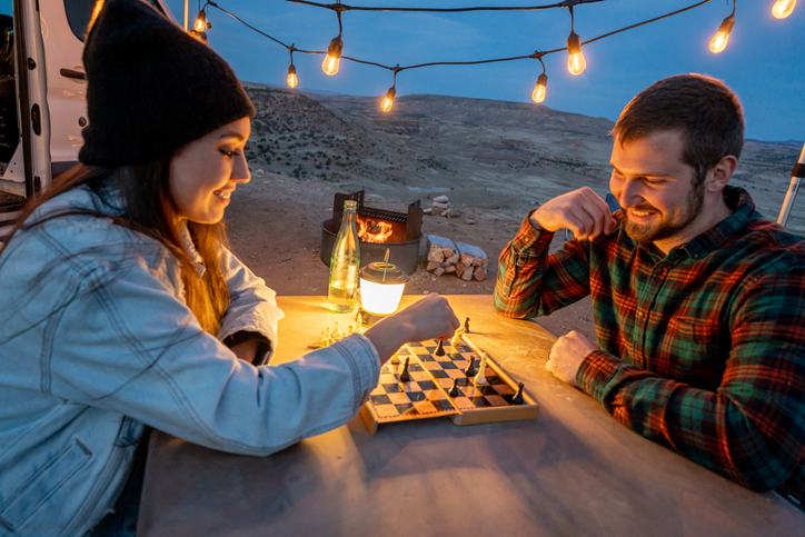 Young Couple Out Camping Playing Chess Together At A Picnic Table 
