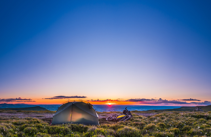 Tent and bikepacking bike camping on mountain ridge at sunset