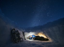 Mature tourist using phone in shelter in the snow at night. Camping in winter mountain alone in nature.