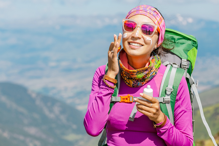 Hiker woman applying sun cream to protect her skin from dangerous uv sun rays high in mountains.
