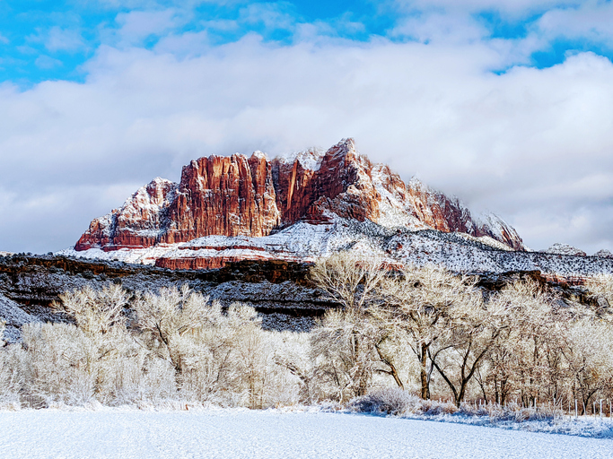 Mt Kinesava in Zion National Park Utah showing snow-covered trees along the Virgin River and pastures below red rocks of sandstone and mesas