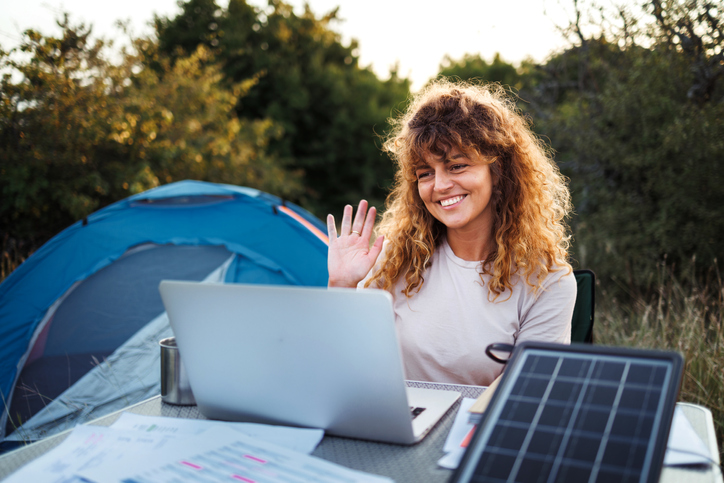 Young woman working on laptop with solar panels near camping tent