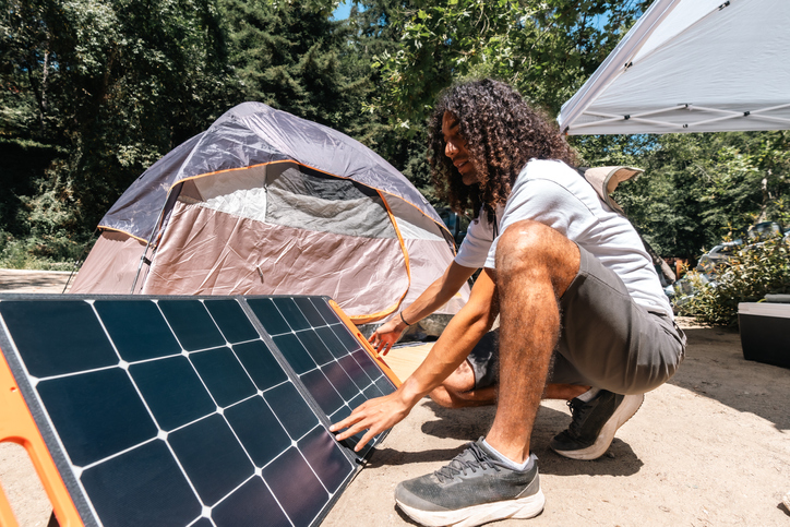 A male camper with curly hair setting up a solar panel at a campsite 