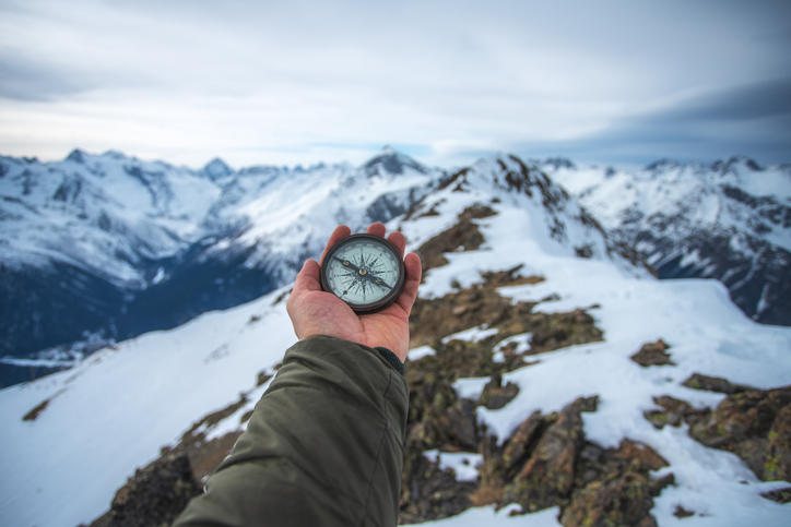 Man stands on top of the mountain and holds compass in hand.