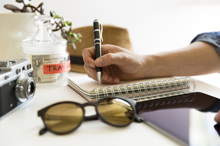 Travel planning with notebook and money saving jar, sunglasses and hat