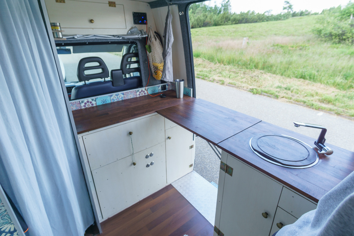 white and brown interior of a self made camper van transporter with cupboard, extendable table and kitchen sink