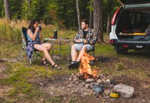 couple sitting in portable chairs drinking tea talking. camping summer activities copy space