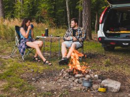 couple sitting in portable chairs drinking tea talking. camping summer activities copy space