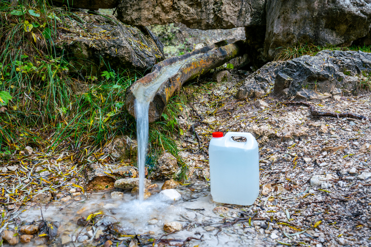 Filling fresh water from a mountain stream in a white plastic can as drinking water for transport and use