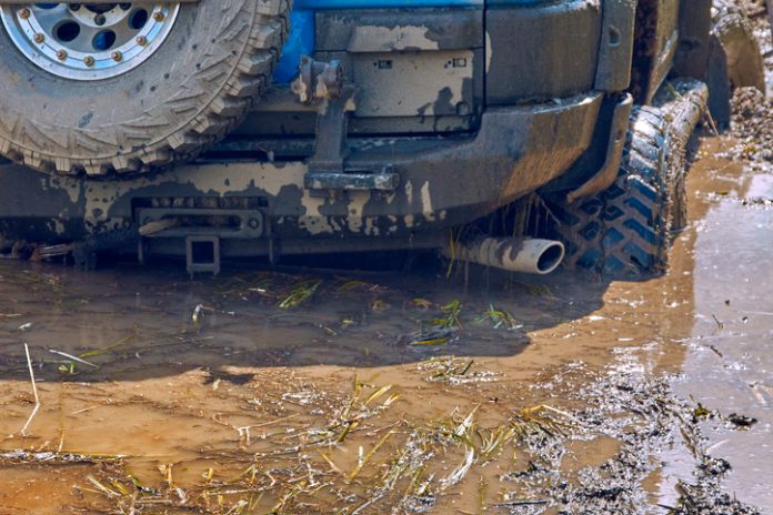 Rear view of a blue 4x4 off-road car stalling in a swamp during extreme competitions.