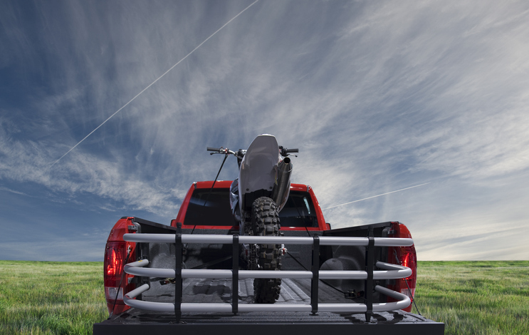 Red pickup truck carrying motocross bike through a field