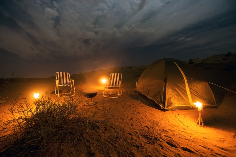 Camping in the desert at night with a tent two chairs and three small torches